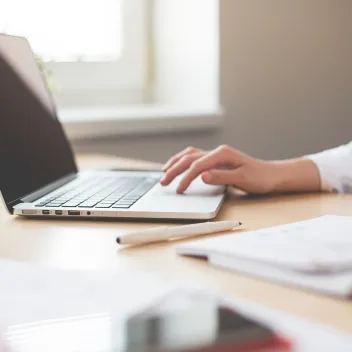 Aufgeklappter Laptop auf Schreibtisch mit arbeitender Person